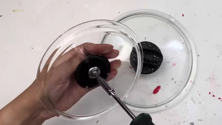 Using a screwdriver to remove the handle of a pot lid.