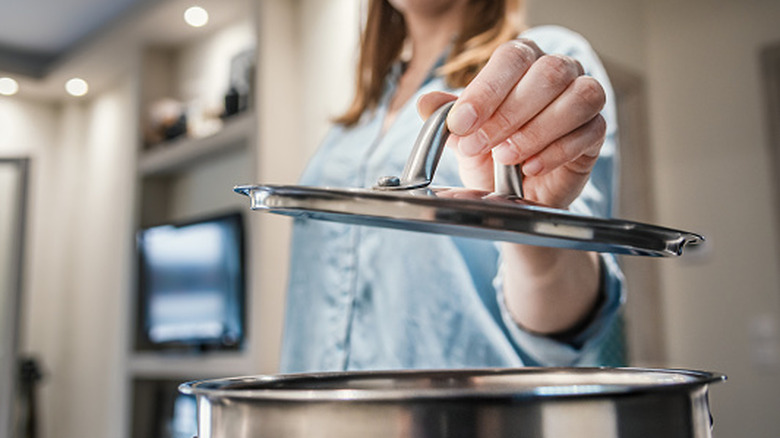 A woman is holding up the lid of a pot.