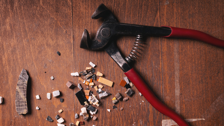 A mosaic tool and ceramic shards sit on a dark wooden table