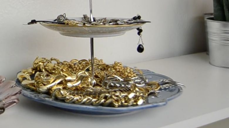 A two-tiered display stand repurposed into a jewelry holder sits on the countertop in a walk-in wardrobe.