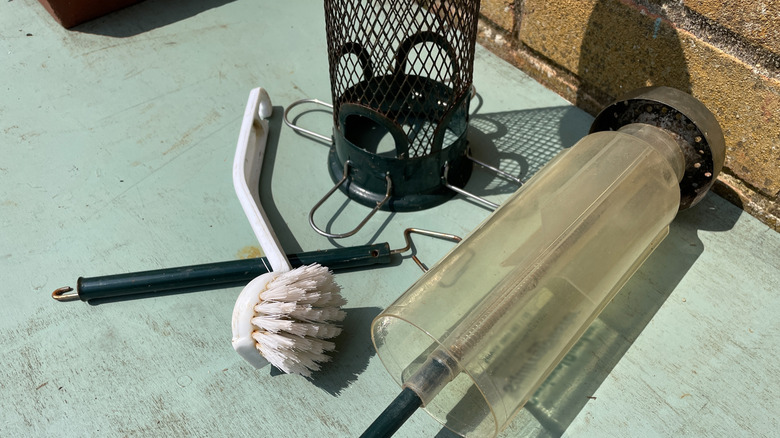 A dismantled bird feeder drying in the sun, next to a cleaning brush
