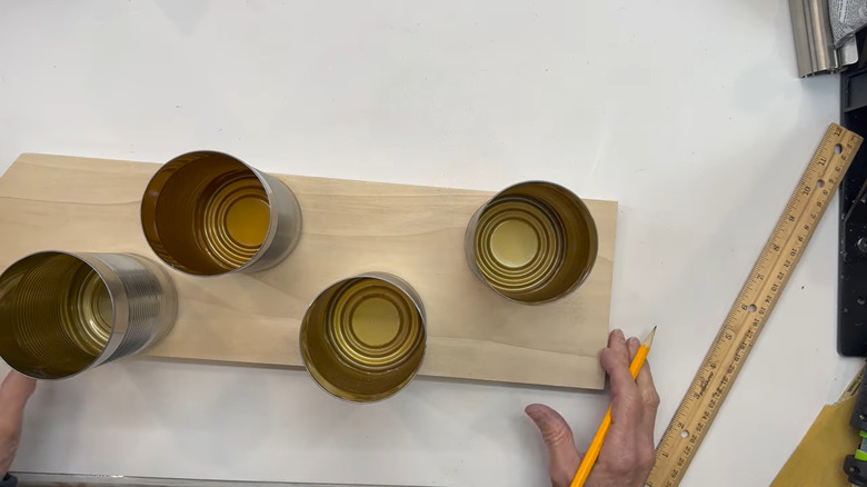A person building a DIY bird feeder using upcycled tin cans and a wooden board.