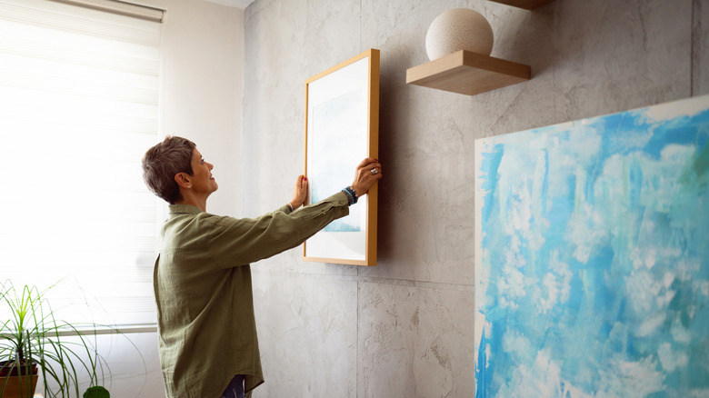 Woman putting up a framed piece of art on a wall next to other art displays