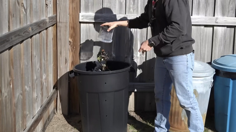 man dumping kitchen scraps into a garbage can compost outside
