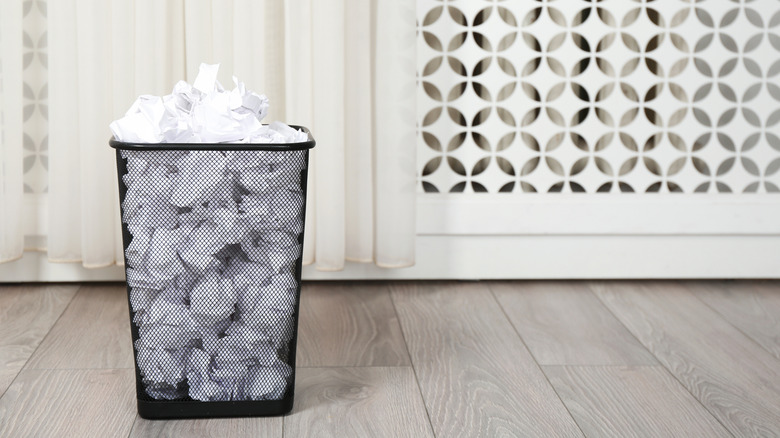 Black wire waste basket full of crumpled paper