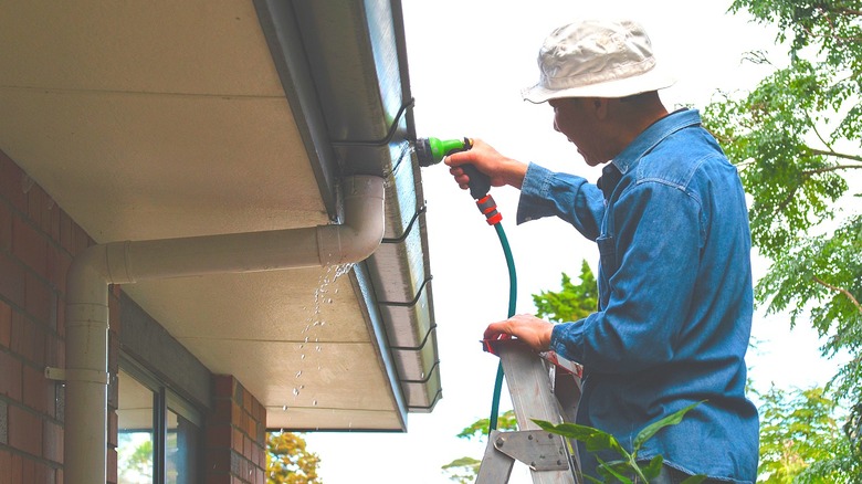 Man on ladder spaying water into downspout from hose