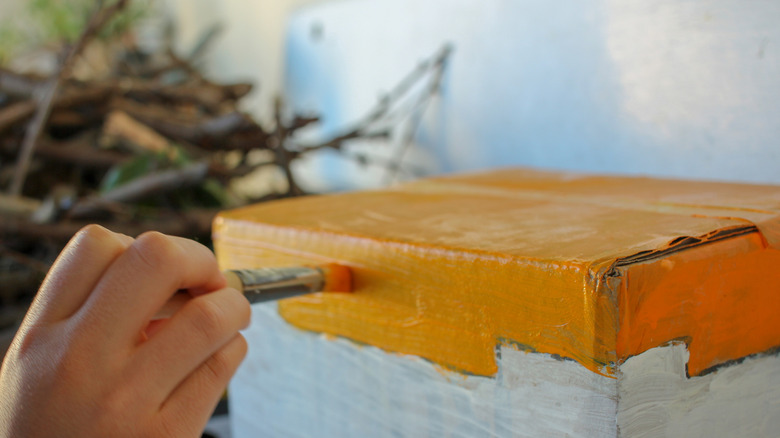 A person paints a cardboard box project with orange paint