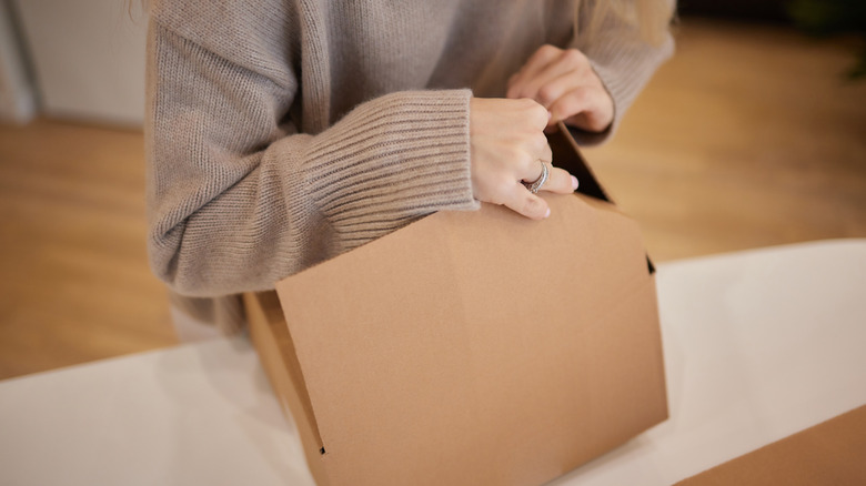 A person folds a medium-sized cardboard box on a table