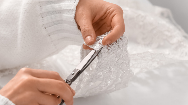 two hands cutting white lace with scissors