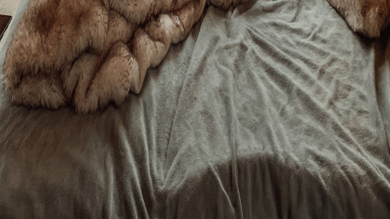 A messy bed in a wood-walled room with a window overlooking snow-covered countryside.