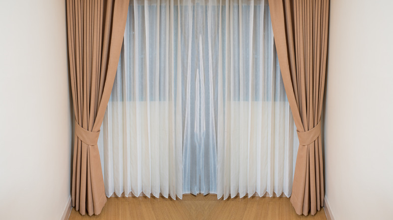 A large set of oversized doors dressed with a white, sheer layer and beige layer of curtains.