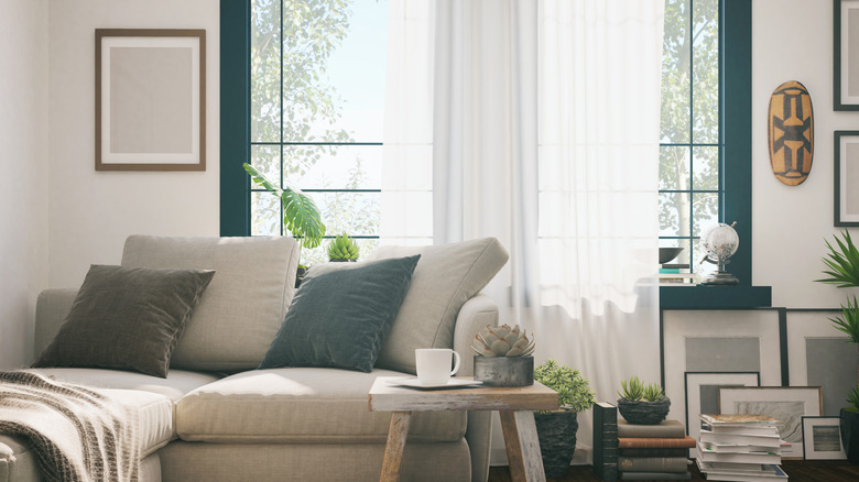 A living room with an oversized window with white curtains and teal window trim.