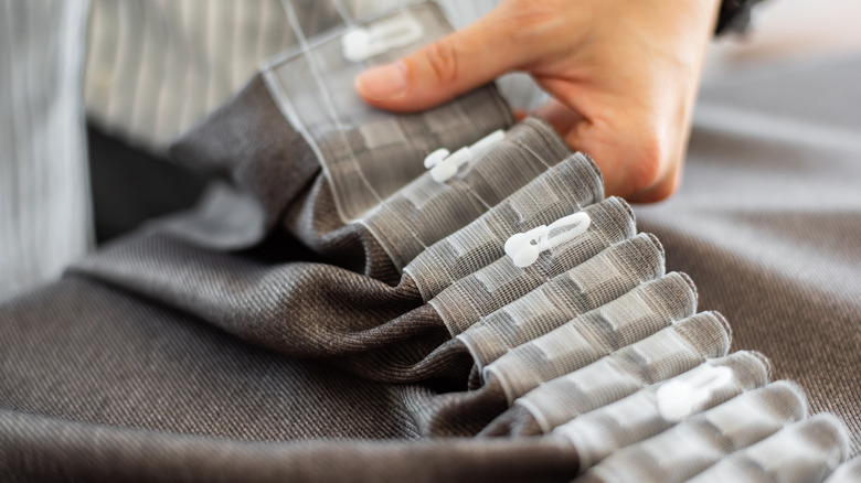 The back of a gray curtain with pleats and pleat hooks at the top of the panel.
