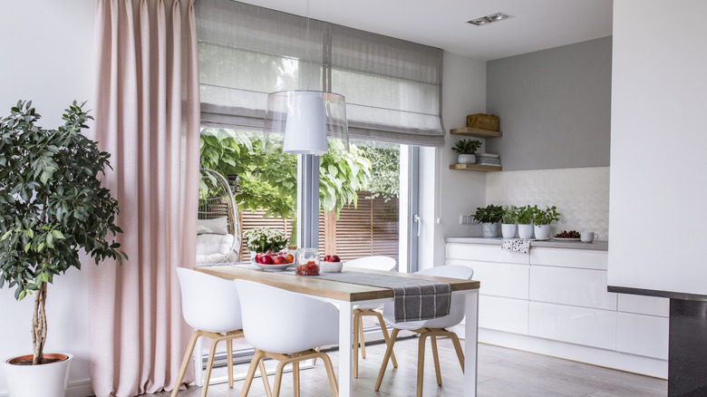 A kitchen and dining space with pink curtains and gray linen roman shades over the sliding door.