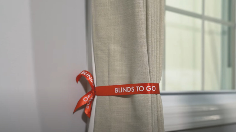 A red ribbon tied around a beige curtain panel.