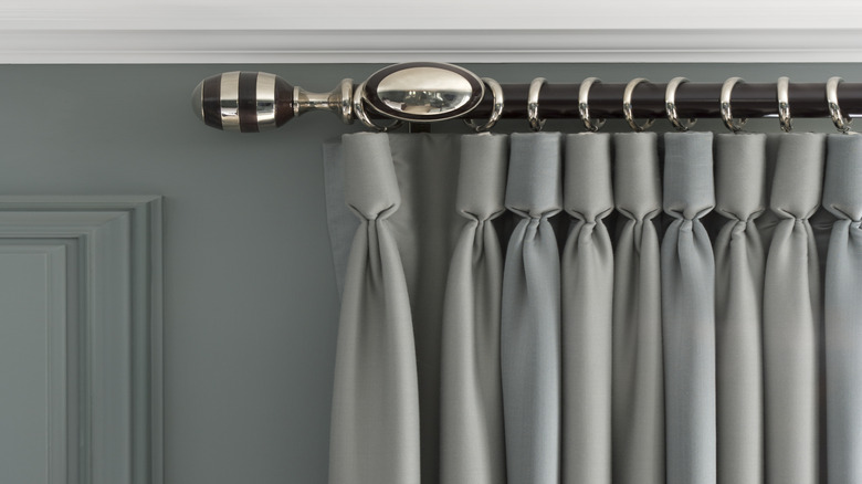 A mixed-metal and wood curtain rod with chrome accents up against a dark gray wall with a gray curtain.