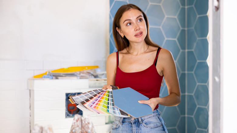 Woman holding paint color swatches and tile in bathroom