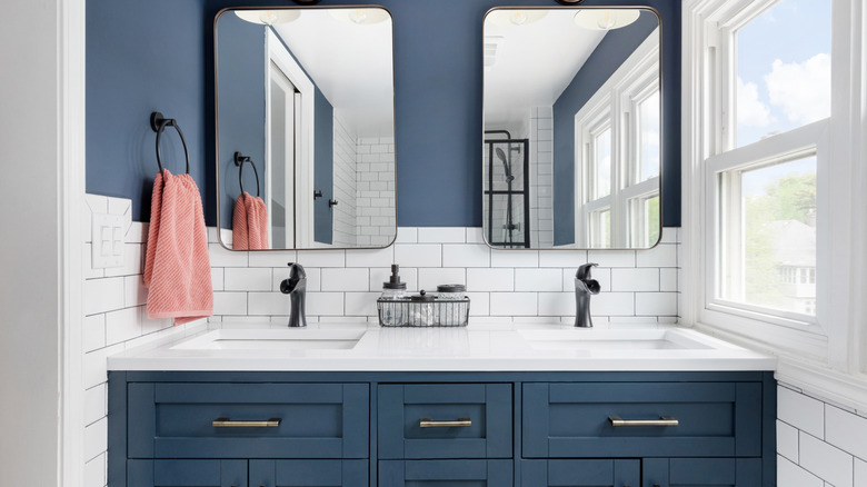 A bathroom with blue walls, white tiles and a blue vanity with double sinks and mirrors above it.