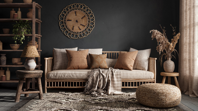 A dark green black painted room with ratten and beige sofa, bookcase, side tables and a circular footstool.
