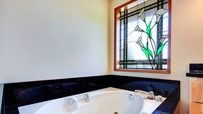 Bathroom with white whirlpool tub, black tile trim around it and stained glass window