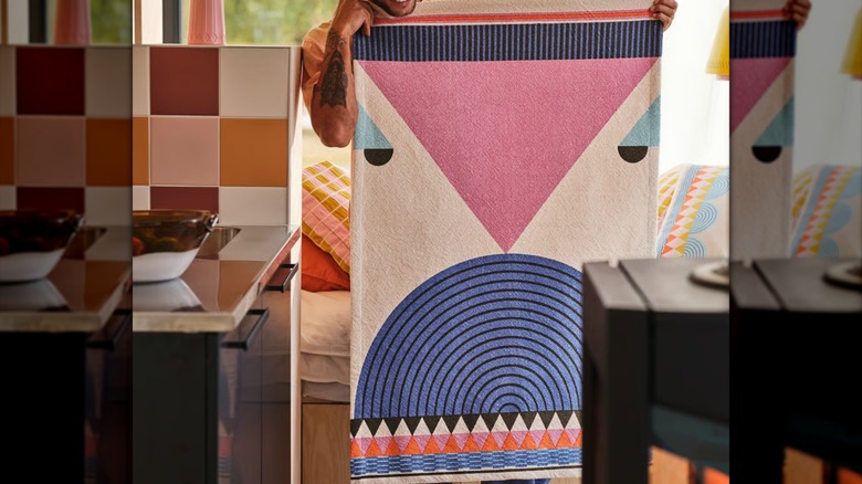 a smiling man holds an OMMJÄNGE hanging tapestry