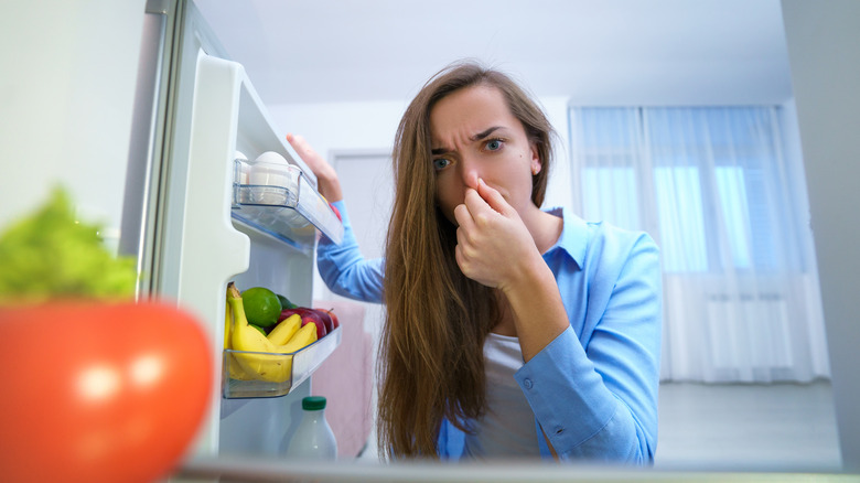 Woman plugging nose looking in refrigerator