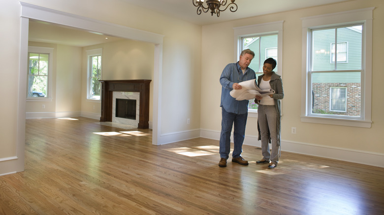 Two people standing in an empty living room looking over plans