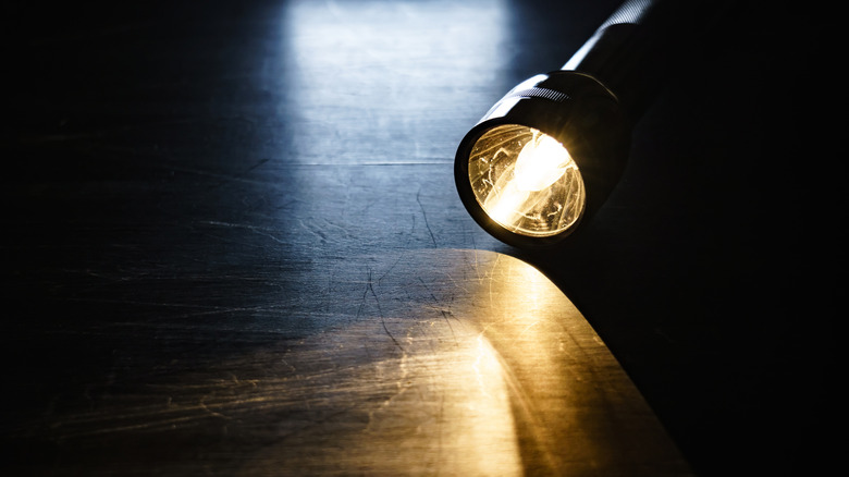Flashlight lying flat on floor casting a beam