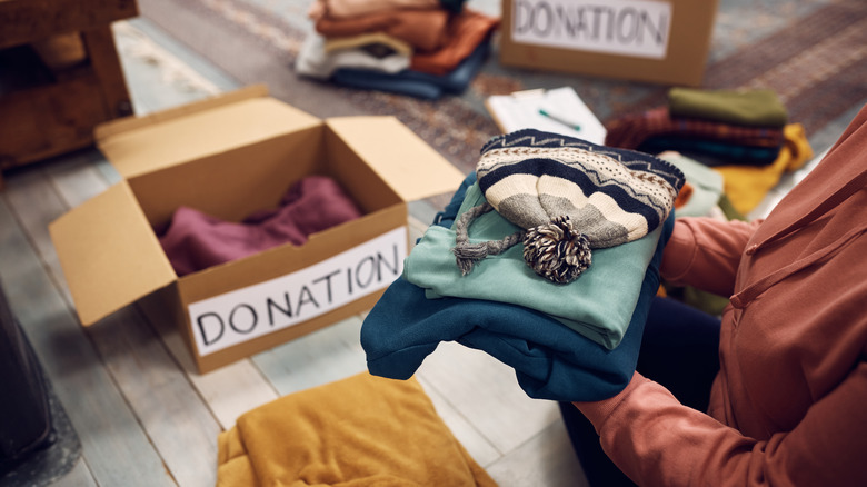 Hands holding a stack of clothes, with items in boxes for donation