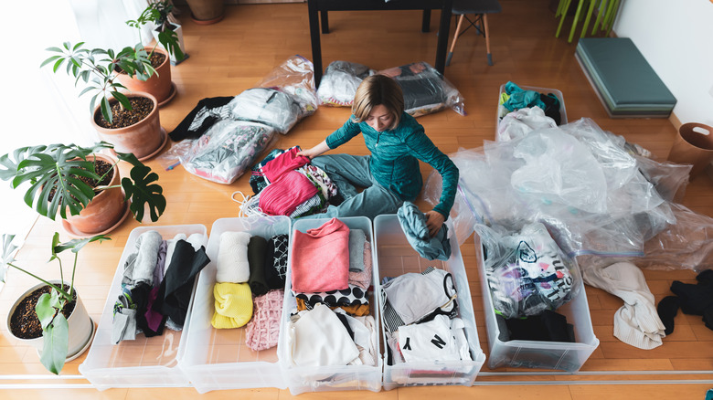 Woman organizing clothing in plastic bins on wood floor