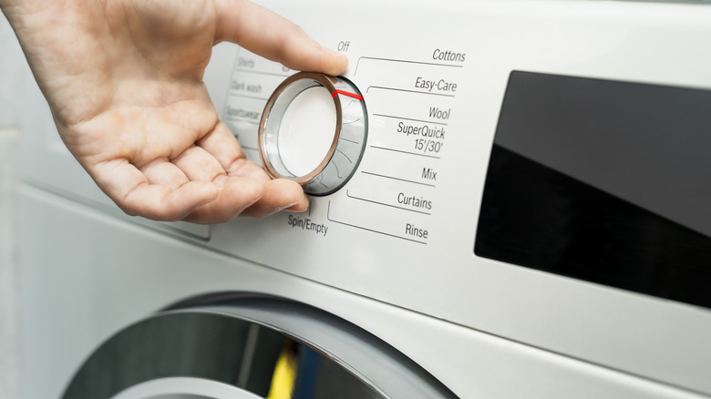 A hand turns the dial to choose a cycle program on a washing machine.