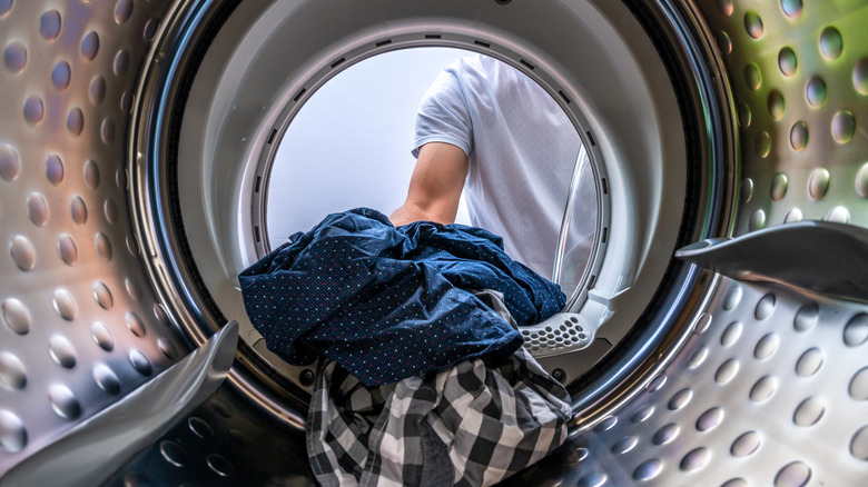A person pulls their clothes out of the drum of a front-loading washing machine.
