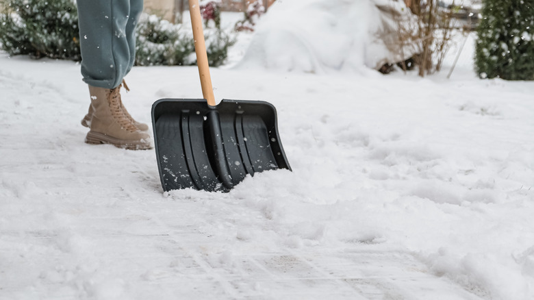 a woman shoveling snow on a home walkway during snowfall