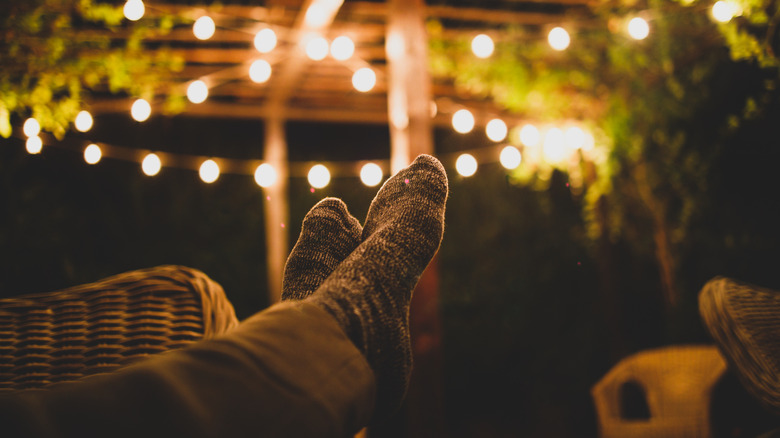 Feet kicked up on a patio at night, with string lights hanging across the ceiling