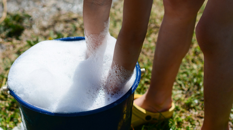 A person mixing foamy detergent in a blue bucket outfoors