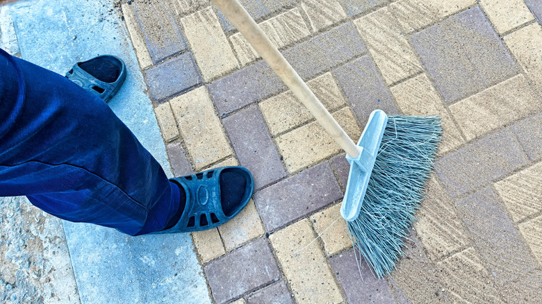man sweeping sand into gaps of pavers on a patio