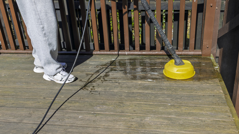 man in gray pants pressure washing a wood deck
