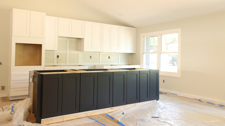 A kitchen build in-progress with white kitchen cabinets and a dark kitchen island