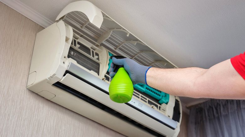 An air conditioner repairperson cleans mold from a ductless unit using a spray bottle.