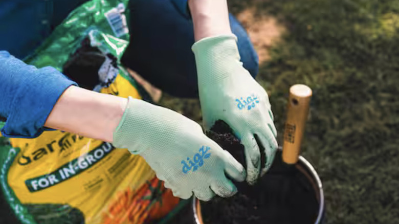 Person digging in bag of potting soil with gardening gloves