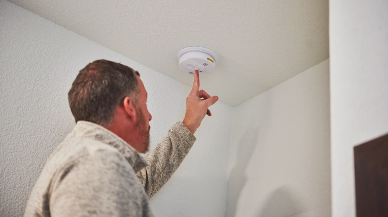 A man checks the battery in a ceiling-mounted carbon monoxide detector