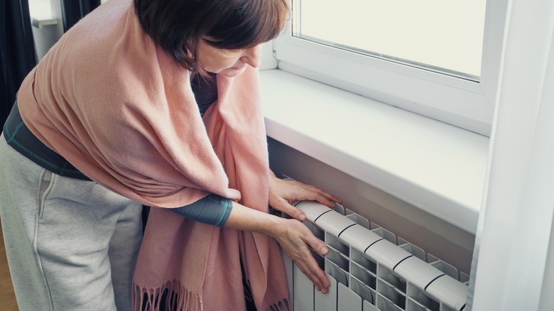 A woman wrapped in a pink blanket putting both her hands on a radiator