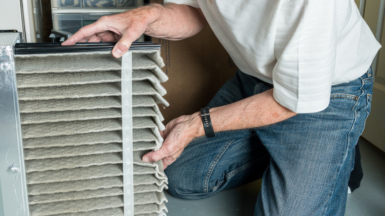 Close-up of a senior caucasian man changing a folded dirty air filter in the HVAC furnace system in basement of home