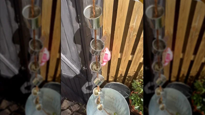 Flower-shaped copper rain chains hanging down into a large metal tub with a fern-like plant on the left