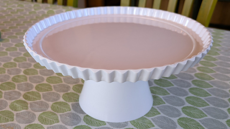 A white cake stand sits on a table covered with a tablecloth.