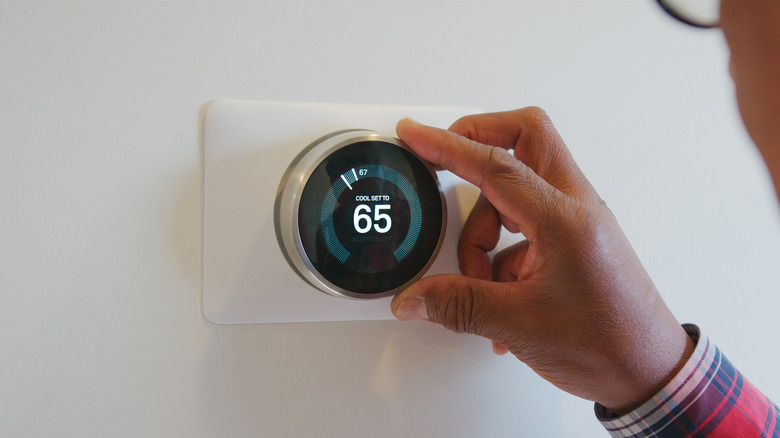 Man adjusting thermostat to cool