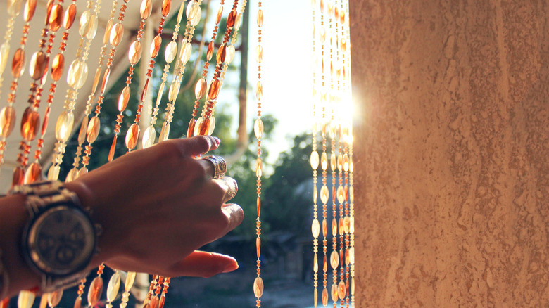 Hand pulling back beaded curtain on window