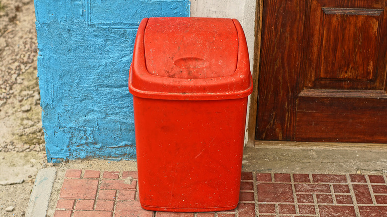 A red trash bin on a tile porch