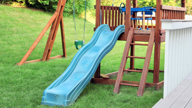 A wooden climbing frame with slide and swing in a garden.