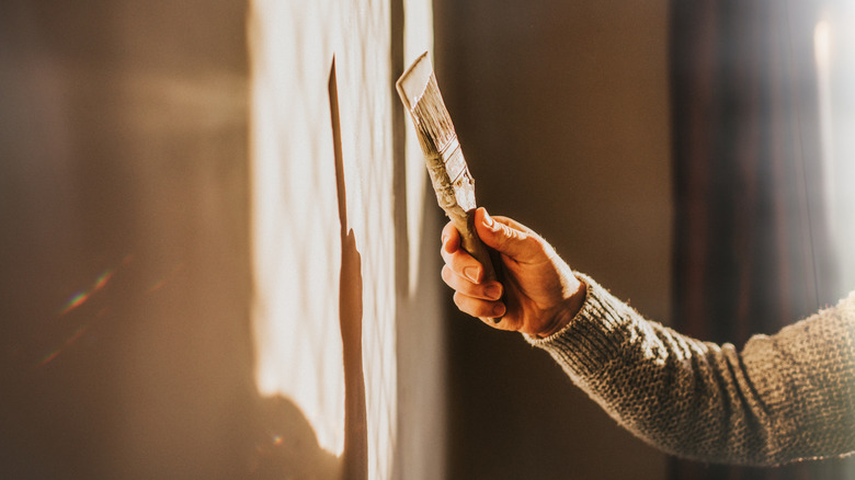 A man painting a wall and holding a paintbrush.
